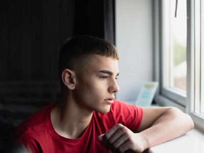 A young person unhappily looks through a window